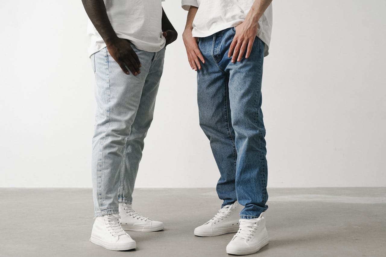 Close-up of two individuals wearing jeans and white sneakers in a minimalist setting.